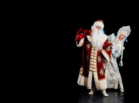 Santa Claus in a red suit and the Snow Maiden in a white fur coat posing against a black backgroundの写真素材
