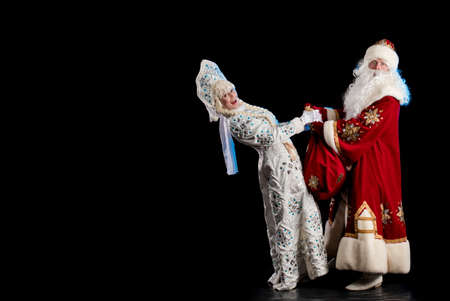 Santa Claus in a red suit and the Snow Maiden in a white fur coat posing against a black backgroundの写真素材