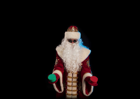 Santa Claus in a red fur coat, with a white beard and a bag of gifts posing on a black backgroundの写真素材
