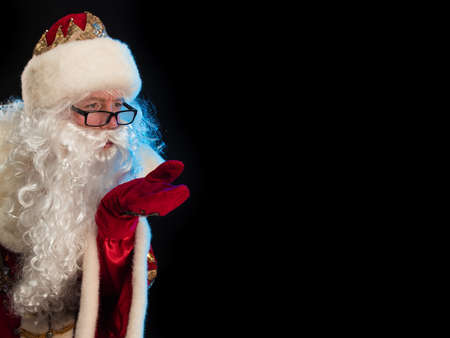 Santa Claus in a red fur coat, with a white beard and a bag of gifts posing on a black backgroundの写真素材