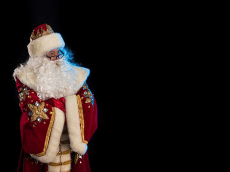 Santa Claus in a red fur coat, with a white beard and a bag of gifts posing on a black backgroundの写真素材