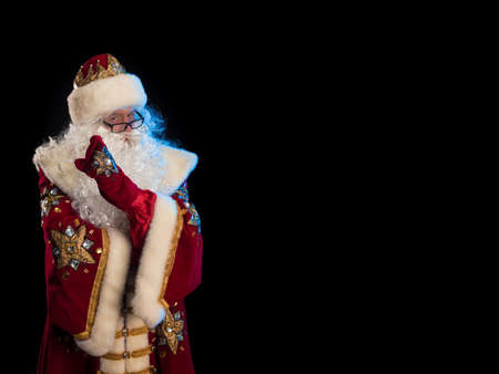Santa Claus in a red fur coat, with a white beard and a bag of gifts posing on a black backgroundの写真素材