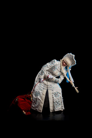 Snow Maiden in a white fur coat, kokoshnik and long hair braids posing on a black background
