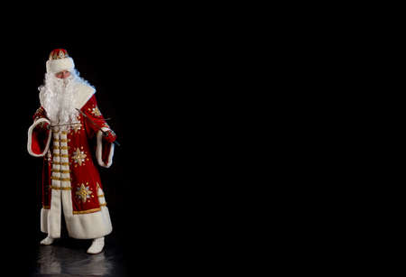 Santa Claus in a red fur coat, with a white beard with two swords in his hands, posing on a black backgroundの写真素材