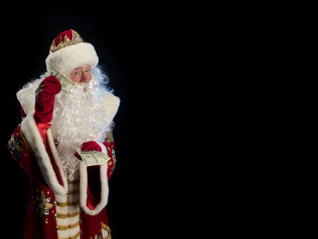 Santa Claus in a red fur coat, with a white beard with two swords in his hands, posing on a black backgroundの写真素材