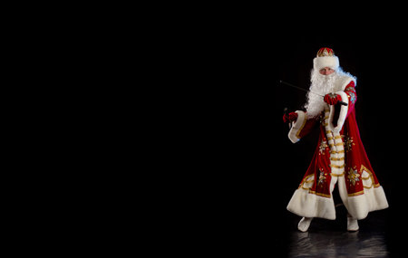 Santa Claus in a red fur coat, with a white beard with two swords in his hands, posing on a black backgroundの写真素材