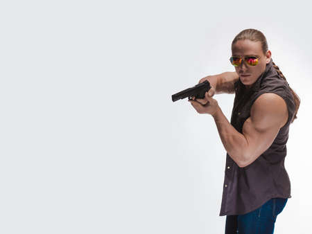 Portrait of a brutal man bodybuilder in sunglasses with a gun on a white backgroundの写真素材