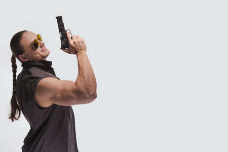 Portrait of a brutal man bodybuilder in sunglasses with a gun on a white backgroundの写真素材