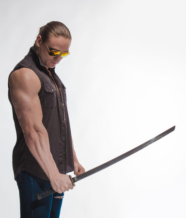 Portrait of a brutal man bodybuilder in sunglasses with a sword on a white background