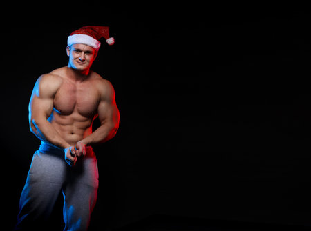 portrait of an athlete bodybuilder posing in cap Santa Claus on a black backgroundの写真素材