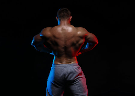 male bodybuilder athlete with naked torso posing against a black background, in red and blue light