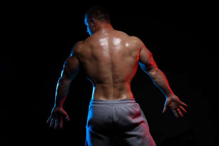 male bodybuilder athlete with torso posing against a black background, in red and blue lightの写真素材