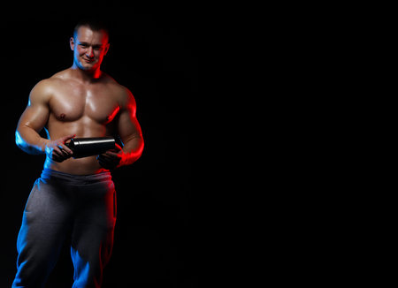 sportsman man bodybuilder with bare-chested with a shaker in hands on a black background, in red and...