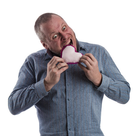 emotional actor man in a gray shirt with a soft toy heart in hands on a white background in studio