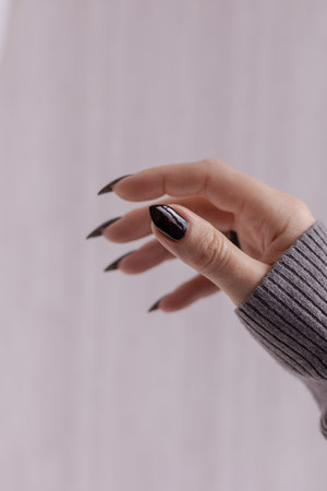 Woman's hands with long nails and gray black manicure with bottles of nail polishの写真素材