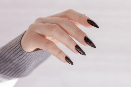 Woman's hands with long nails and gray black manicure with bottles of nail polishの写真素材