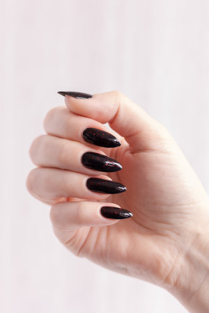 Woman's hands with long nails and gray black manicure with bottles of nail polishの写真素材