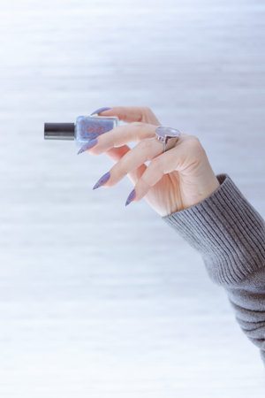 Female hand with lilac purple long nails and nail polish bottle