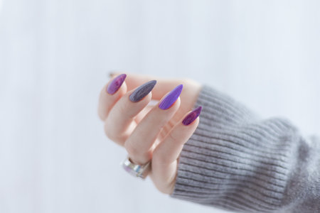 Female hand with lilac purple long nails and nail polish bottleの写真素材