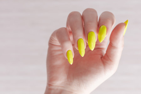 Female hand with long nails and a bottle of bright neon yellow nail polishの写真素材