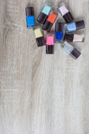 Collection of multi-colored bottles of nail polish. Layout for design on a gray background and a wooden table.の写真素材