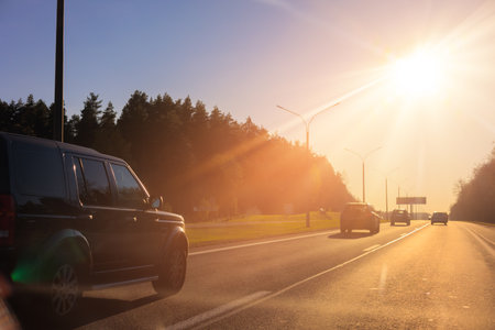 Autumn landscape and view of the road with cars. Orange evening sun and reflections on cars.の写真素材