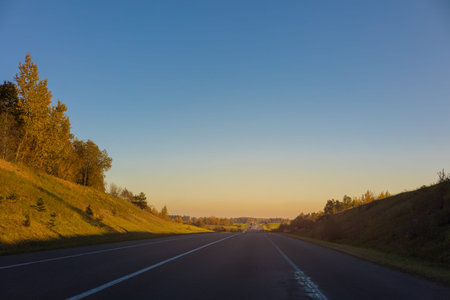 Autumn landscape and view of the road with cars. Orange evening sun and reflections on cars.の写真素材