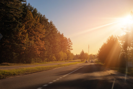 Autumn landscape and view of the road with cars. Orange evening sun and reflections on cars.の写真素材