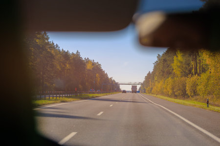 Autumn landscape and view of the road with cars. Orange evening sun and reflections on cars.