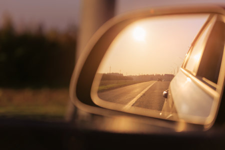The sun is reflected in the mirror, evening road. View in the side rear view mirror of a red car driving along the highway and streetの写真素材