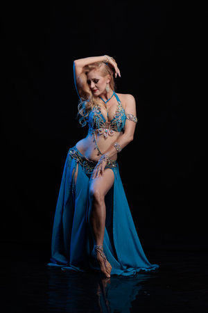 Woman in a blue costume oriental dancer posing and dancing on a black backgroundの写真素材