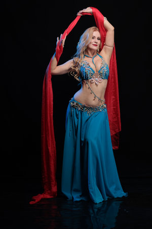 Woman in a blue costume oriental dancer posing and dancing on a black backgroundの写真素材
