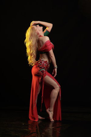 Dancer girl with long hair in red oriental costume posing and dancing on black backgroundの写真素材