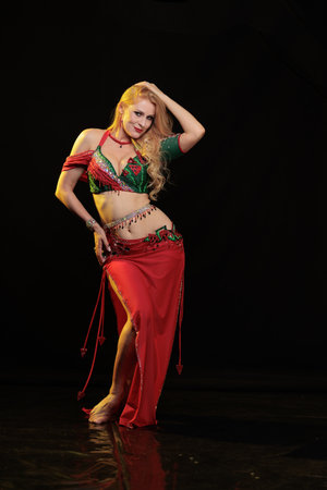 Dancer girl with long hair in red oriental costume posing and dancing on black backgroundの写真素材