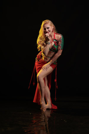 Dancer girl with long hair in red oriental costume posing and dancing on black backgroundの写真素材