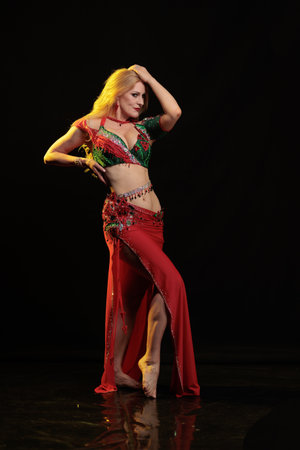Dancer girl with long hair in red oriental costume posing and dancing on black backgroundの写真素材