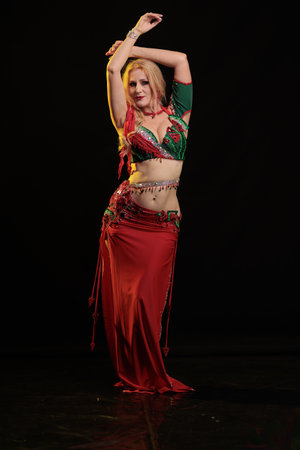 Dancer girl with long hair in red oriental costume posing and dancing on black backgroundの写真素材