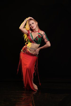 Dancer girl with long hair in red oriental costume posing and dancing on black backgroundの写真素材