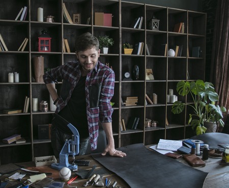 Man leather worker stands near wooden table with piece of leatherの写真素材