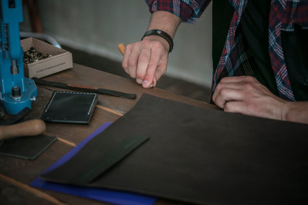 Leather manufacturer working with tool on wooden table with leather
