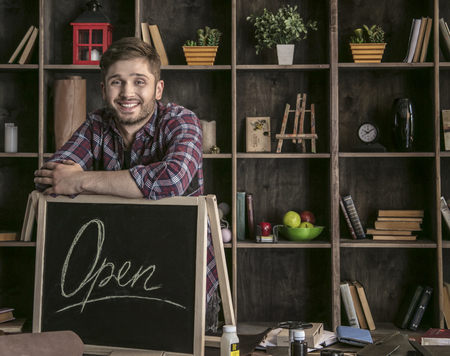 Young smiling man leather worker standing near open sign at table with toolsの写真素材