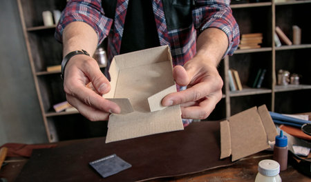 Young man leather maker manually assemble cardboard packaging box for products