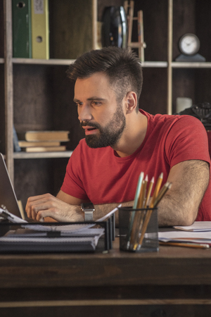 Young businessman sitting behind desk with open laptopの写真素材