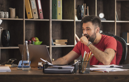 Young businessman sitting in studio with laptop and surprising by amazing newsの写真素材