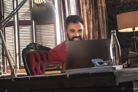 Young business man sitting in cozy dark office in chair and looking laptopの写真素材