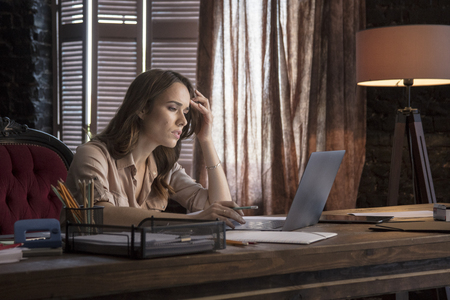 Young business woman sitting at desk holding pencil and carefully watches newsの写真素材