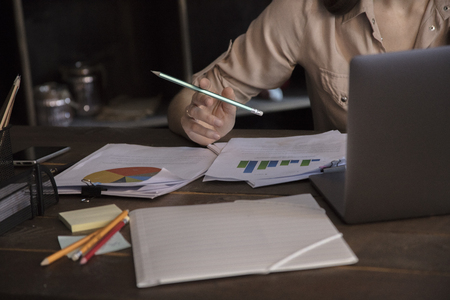Business woman holding pencil and working on laptop at table with documentsの写真素材