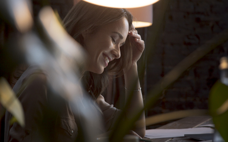Young beautiful business woman sitting at table and laughing with closed eyesの写真素材