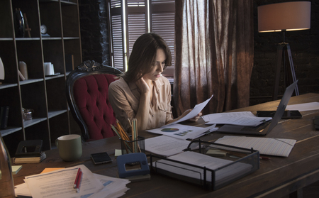 Businesswoman sitting in chair behind table with holding in hand documentsの写真素材