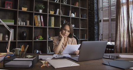 Businesswoman sitting in chair and viewing document with serious expression on faceの写真素材